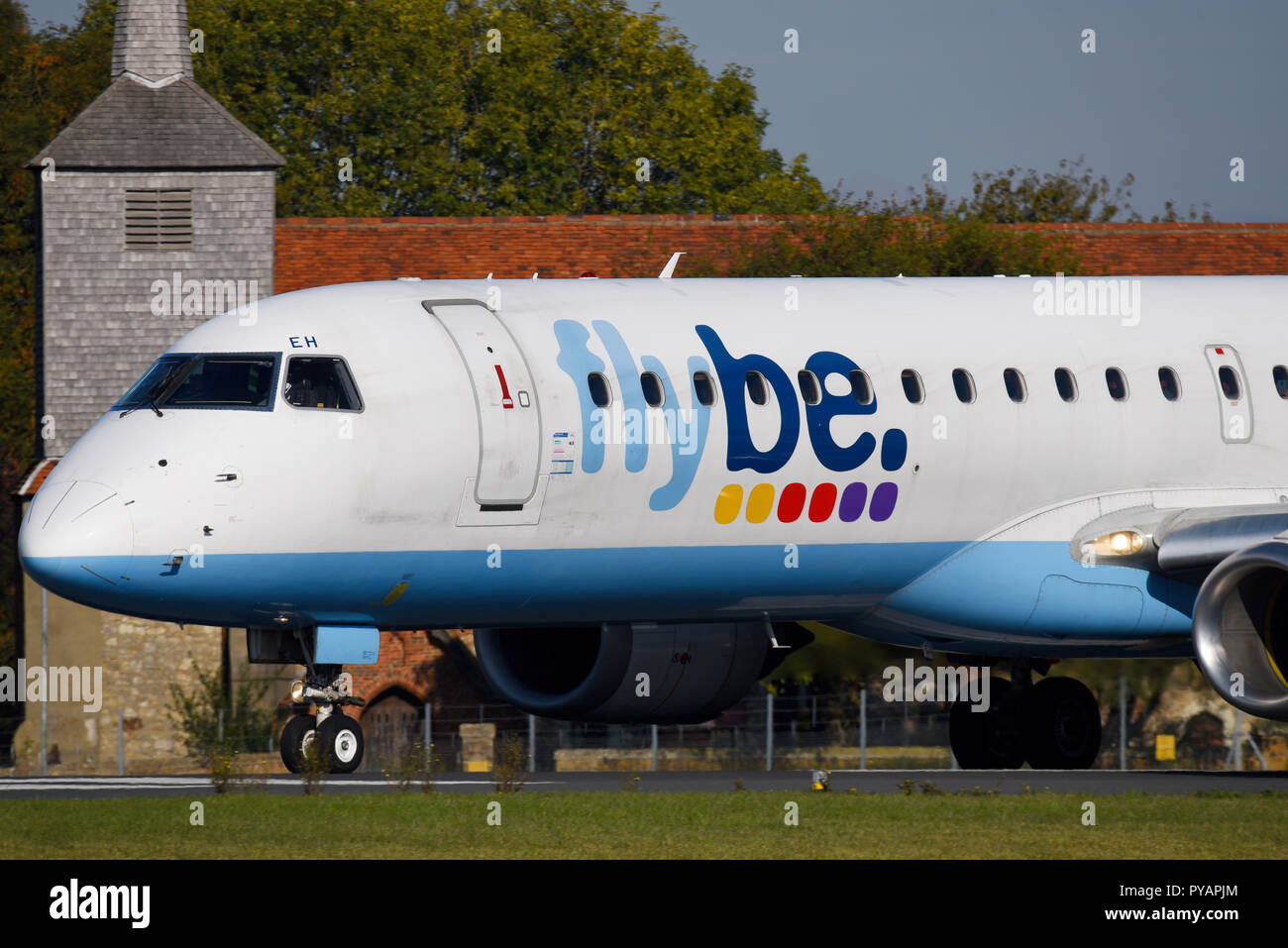 flybe jet plane. Embraer ERJ195 G-FBEH passing the church after landing at London Southend Airport, Essex, UK Stock Photo