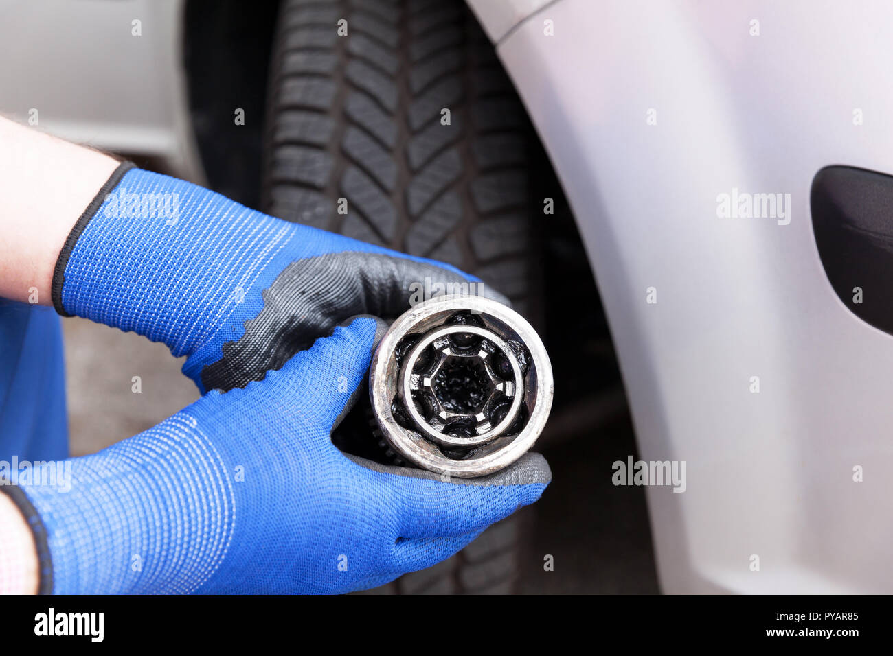 Automechanic, wearing blue work gloves, holding an old constant