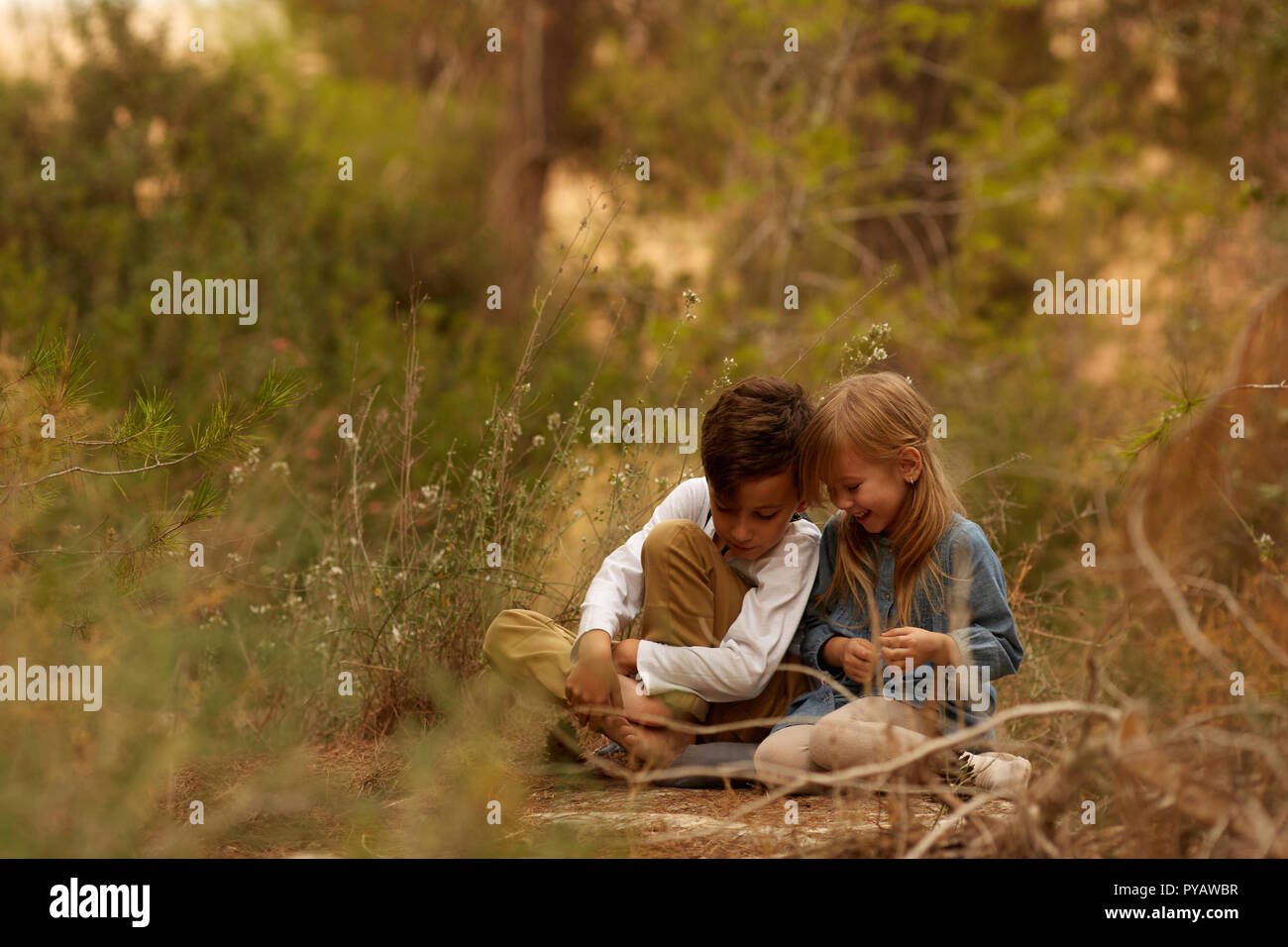 Cute boy and girl touching heads while sitting on ground in majestic countryside Stock Photo