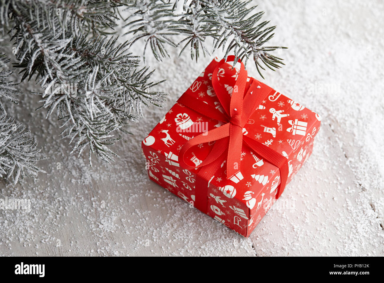 Christmas red gift box with festive pattern and ribbon under snowy fir ...