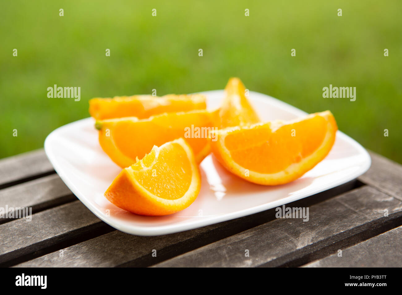 orange wedges on white plate set on wood surface with green background Stock Photo