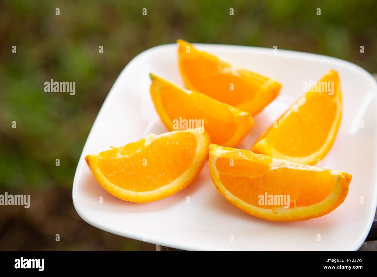orange wedges on white plate set on wood surface with green background Stock Photo