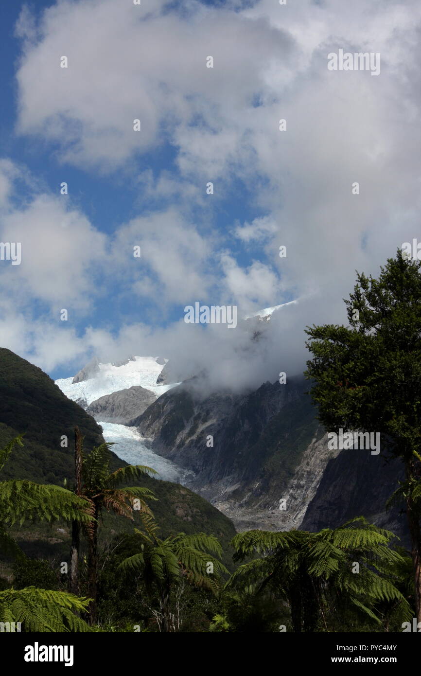 Franz Josef Glacier, with low cloud lifting against a blue sky, showing the slopes of the mountain ice river path. a New Zealand tourisn site Stock Photo