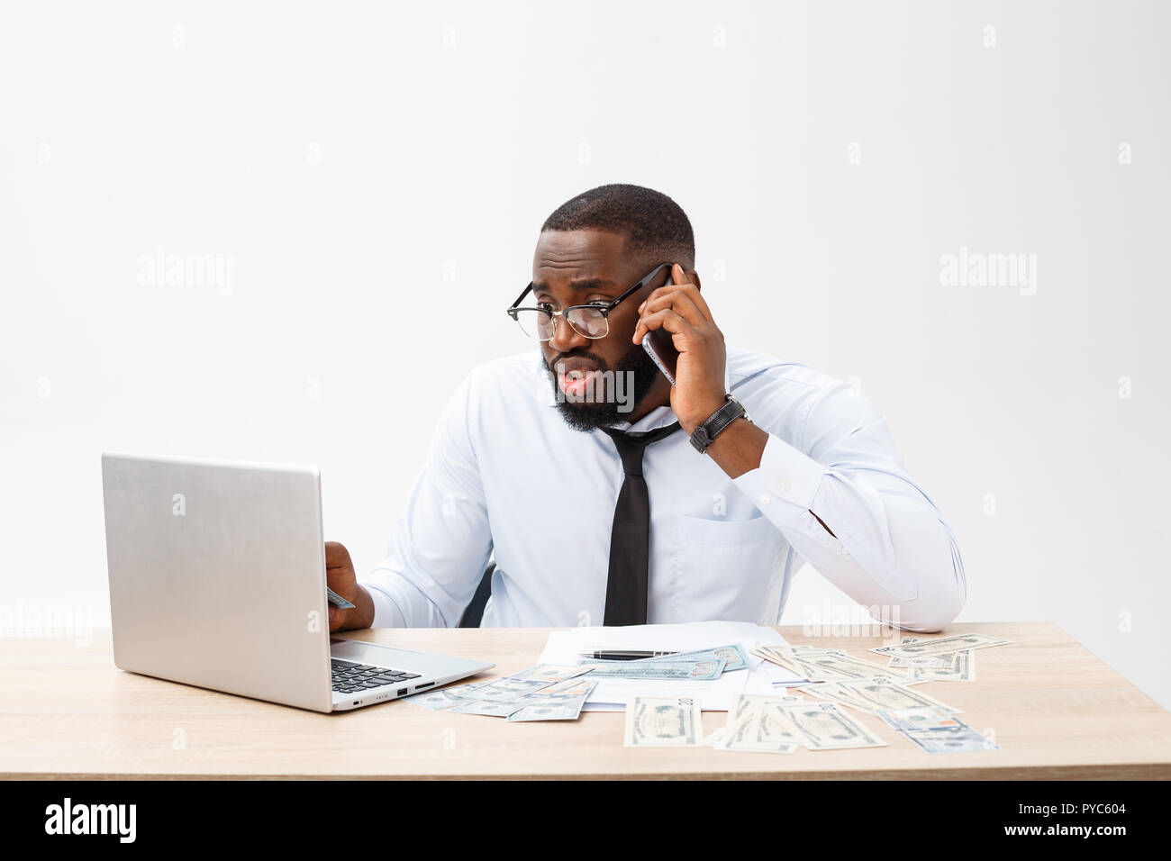 Irritated dark skinned young male enterpreneur being on working place feels very stressed and angry as cannot manage to do all work, surrounded with modern gadgets, looks in displeasure away Stock Photo