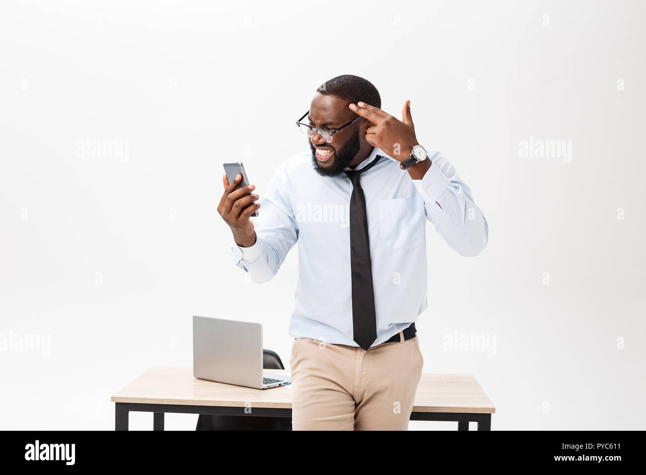 Irritated dark skinned young male enterpreneur being on working place feels very stressed and angry as cannot manage to do all work, surrounded with modern gadgets, looks in displeasure away Stock Photo