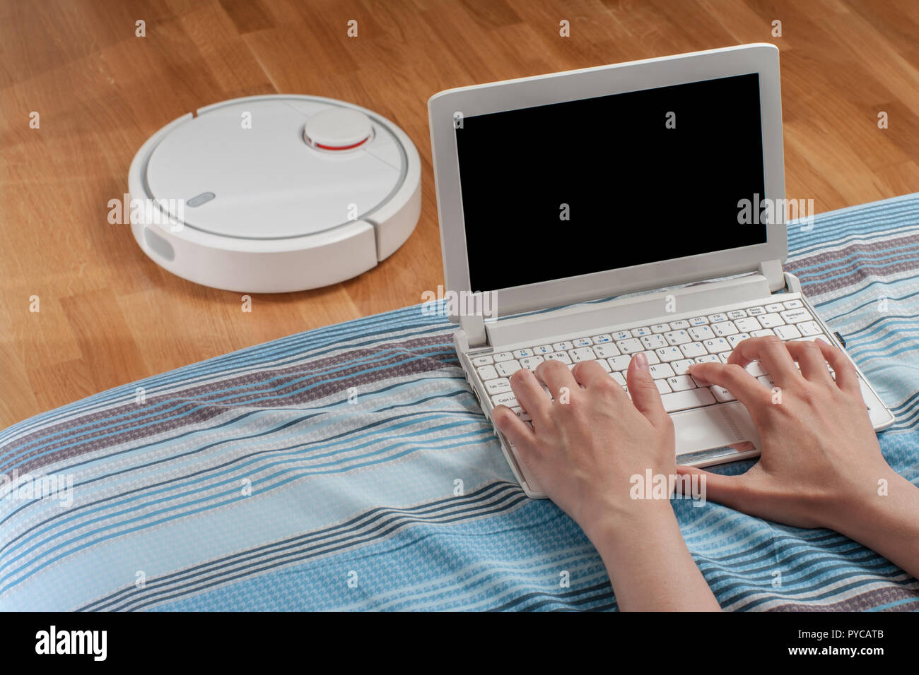 woman works at computer in living room while robot vacuum cleaner ...