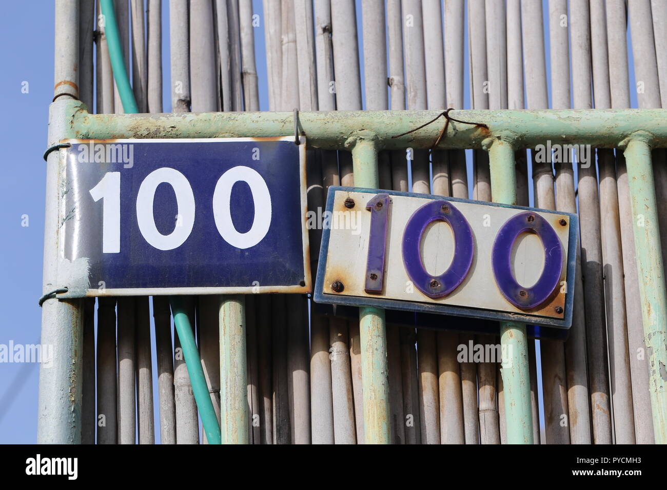 100 Sign. Two No. Letters 100 on house Signs. House no. 100 in two old street signs, Israel. Double number hundred home signs on a metal house fence. Stock Photo