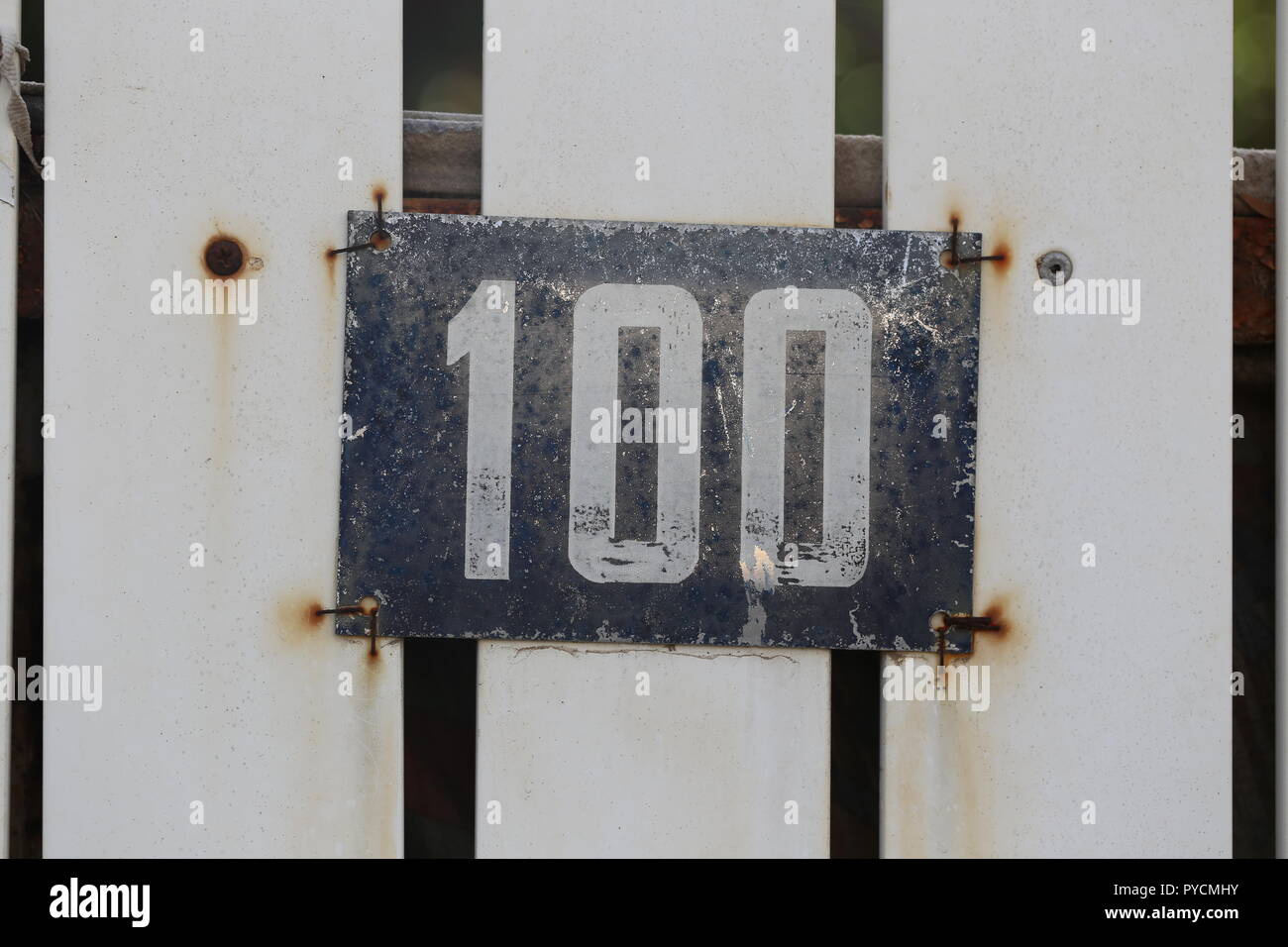 Number 100 Sign. House no. 100 in an old street sign, Israel. The number hundred of home sign, in white latin printed digits in peeling paint. Stock Photo