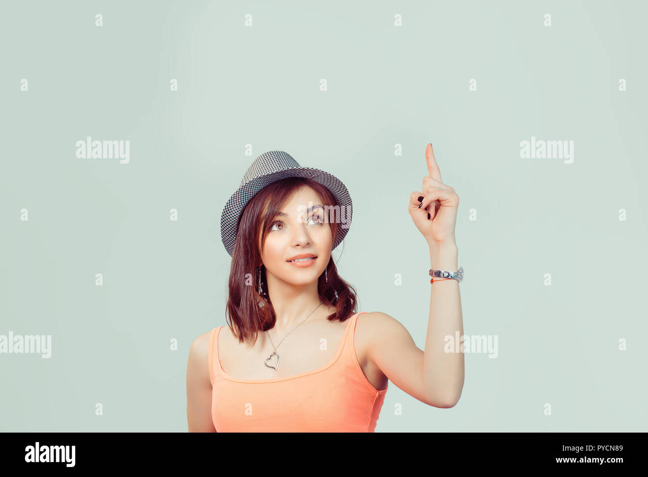 Look up here. Beautiful funny confused woman presenting showing copy space above head with index finger hand isolated light green yellow background. B Stock Photo