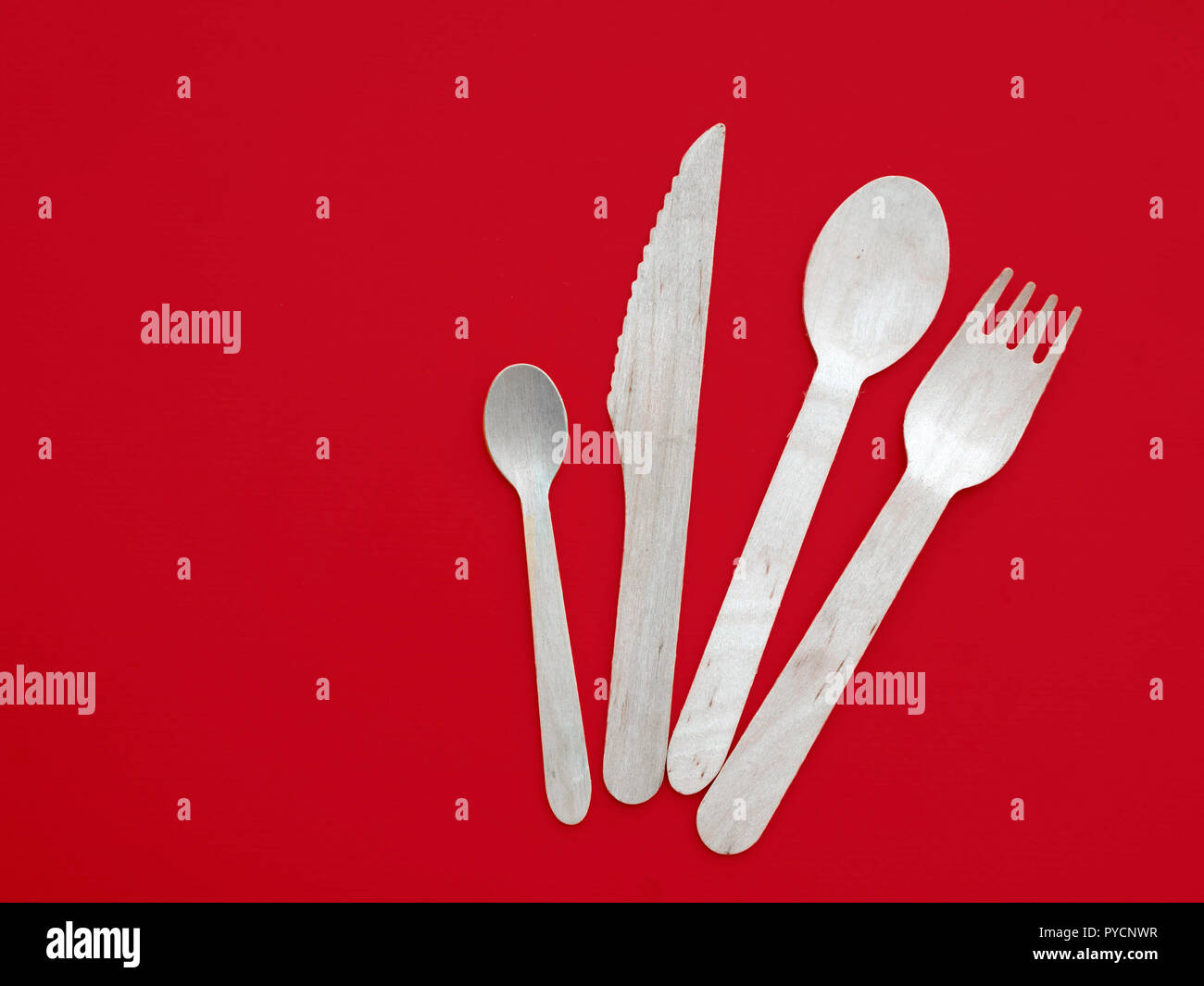 Wooden spoon, knife and fork isolated on white background. Eco friendly disposable cutlery on red. Stock Photo