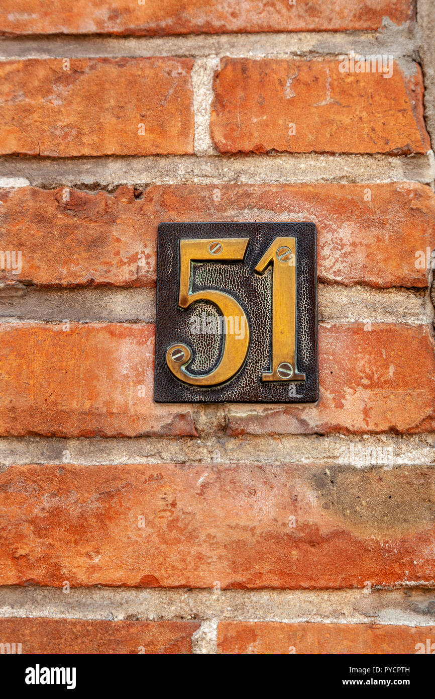 House number fifty-one 51 in pressed metal polished brass and black screwed to brickwall from Sweden or Belgium Stock Photo