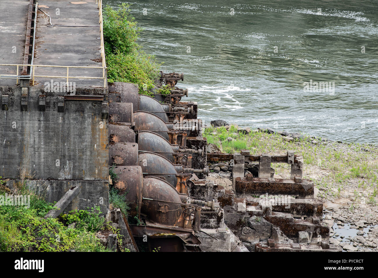 Abandoned old falling apart rusty factory on the Willamette river. Rusting industrial water pumps next to the concrete station. Stock Photo