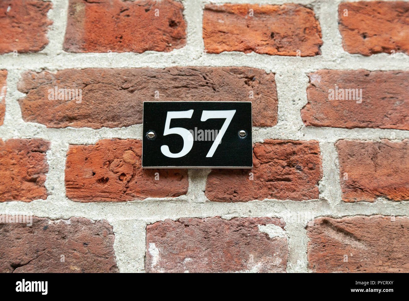 House number fifty-seven 57 in white on metal black plaque screwed to bricks from Sweden Stock Photo