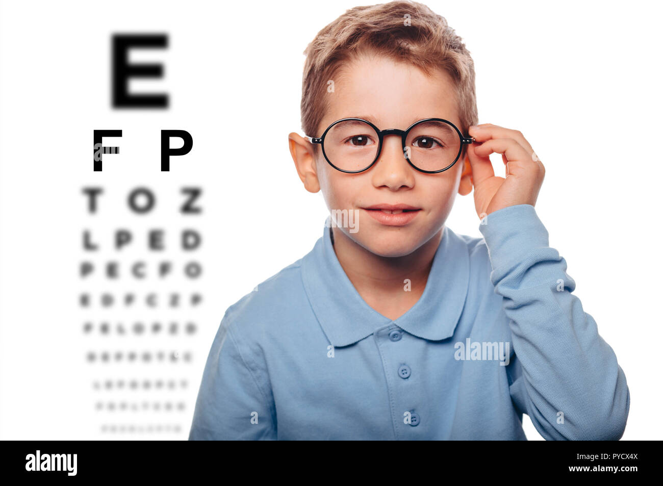 little boy ajusting his eyeglasses standing beside an eye test. Concept