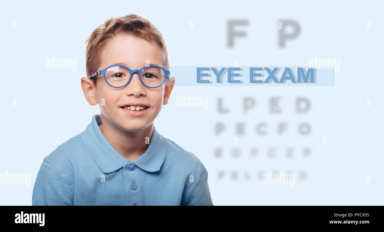 little happy boy wearing eyeglasses standing beside an eye test
