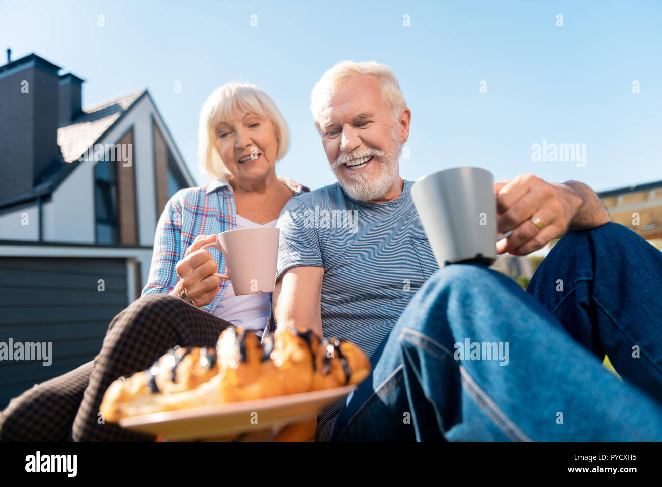 Caring retired husband bringing some biscuits for wife while drinking tea Stock Photo