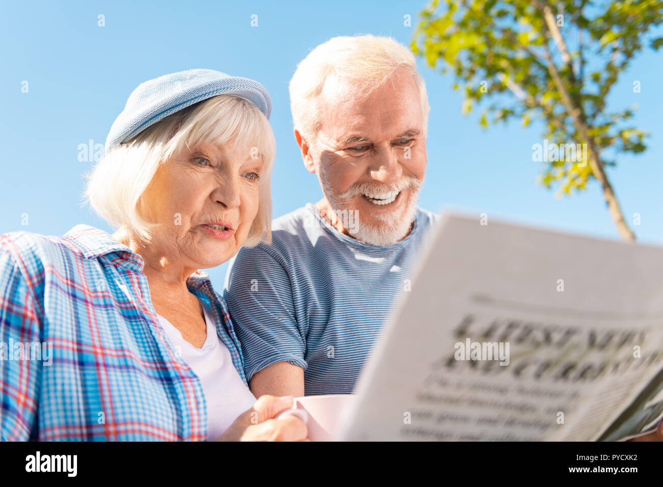 Grandmother and grandfather seeing story about their grandchildren in newspaper Stock Photo