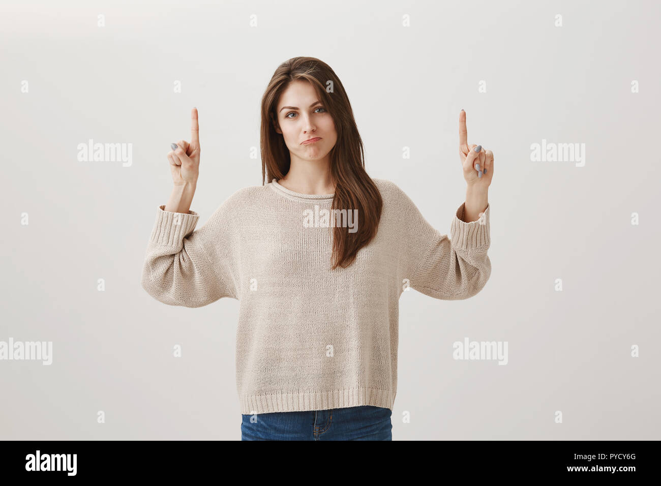 It could be worse. Portrait of gloomy bothered slender female in casual outfit pointing up with raised index fingers, making sad smile and gazing at camera, losing or upsetting cause of bad weather Stock Photo