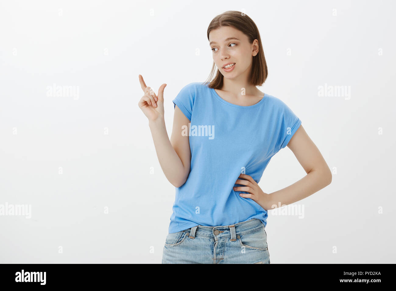 Unimpressive size for me. Portrait of scorning good-looking confident woman in blue t-shirt, holding hand on hip and looking at arm while shaping small or tiny thing, being unimpressed Stock Photo