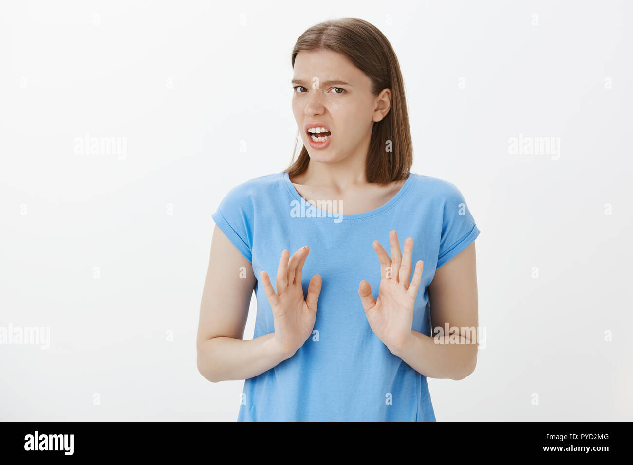 Portrait of displeased and disgusted european woman in blue t-shirt, shaking palms in rejection gesture, disliking idea and declining it, expressing antipathy and disappointment over grey wall Stock Photo