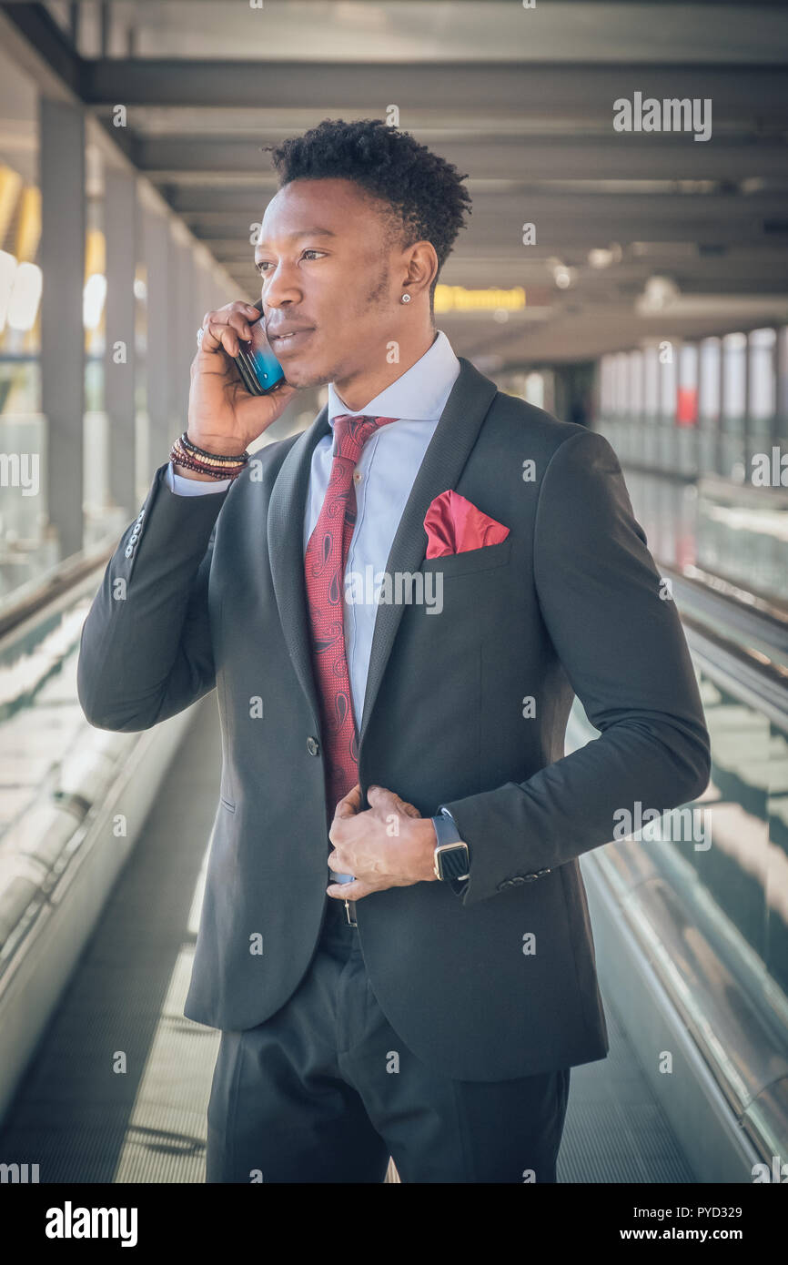 close up of one young and attractive black businessman going to the airport wearing a black suit with a red tie he is smiling and talking by telephon PYD329