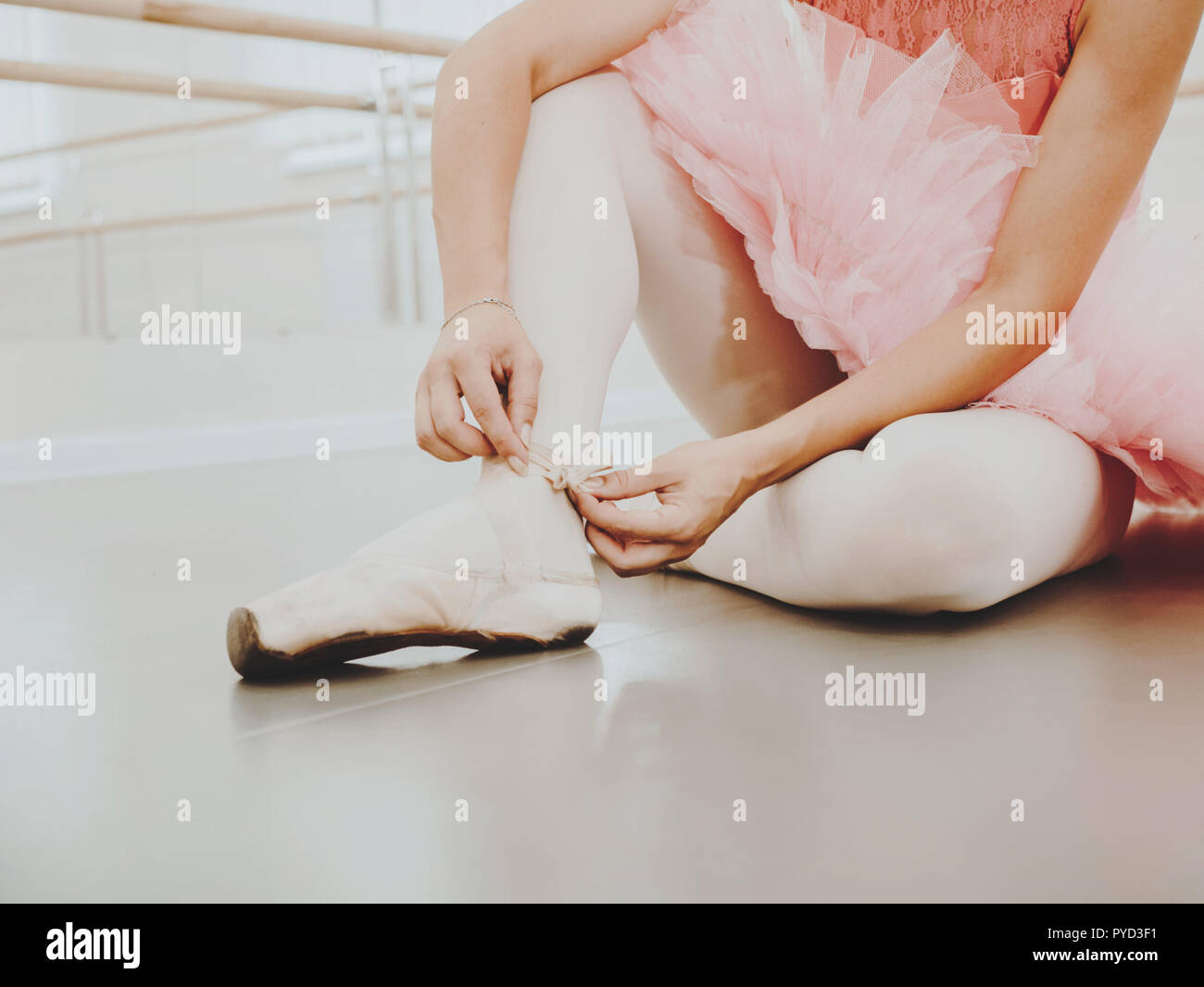 Young ballerina in pink tutu costume wraps white silk ribbons of soft