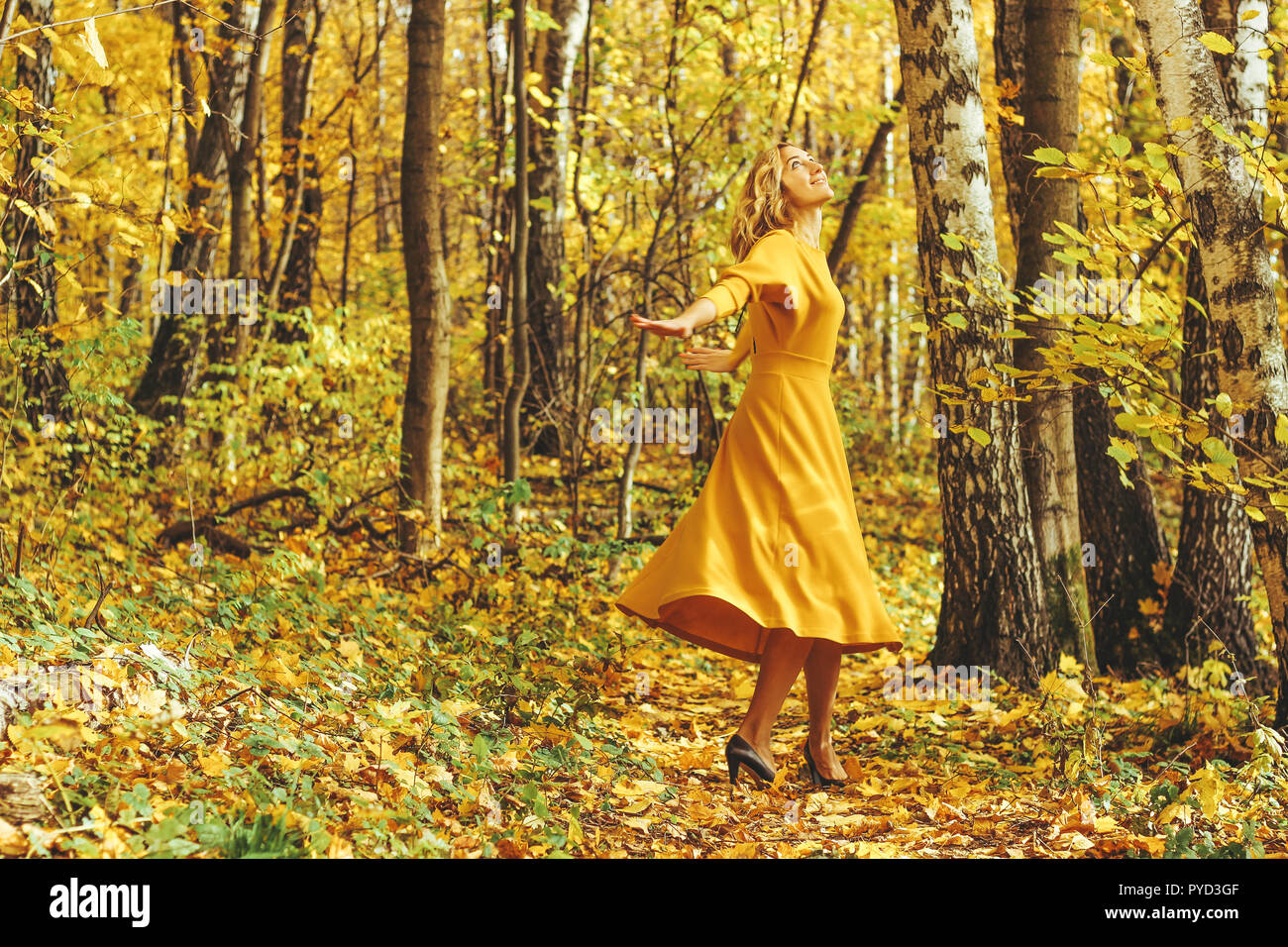 Young beautiful girl in a yellow long dress walks in autumn park with ...