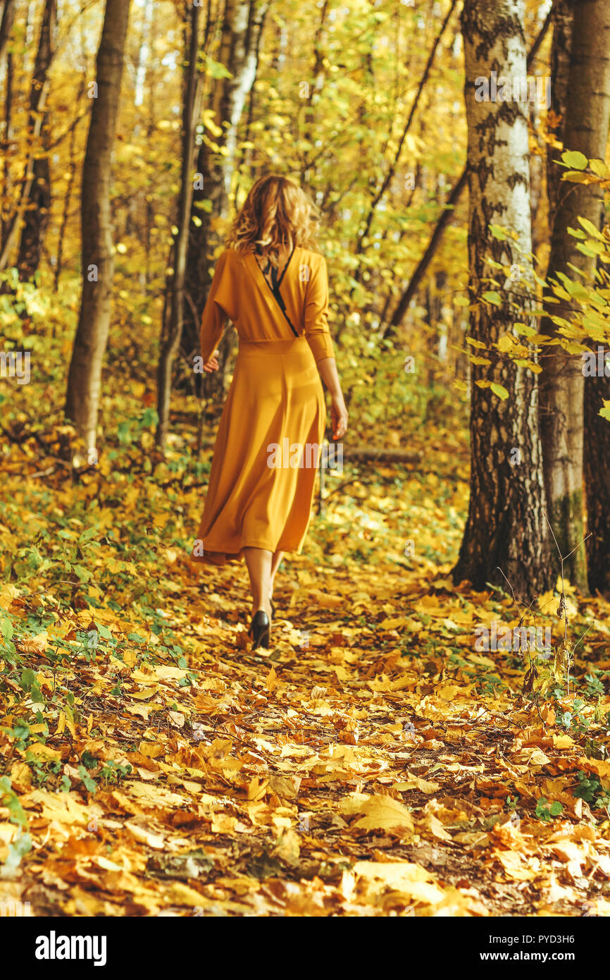Young beautiful girl in a yellow long dress walks in autumn park with ...