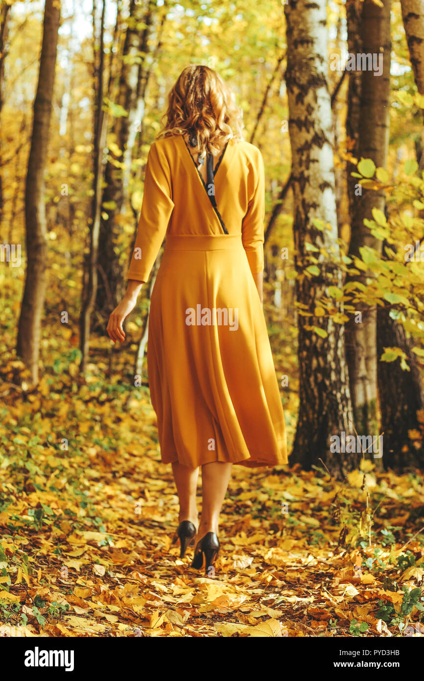 Young beautiful girl in a yellow long dress walks in autumn park with ...