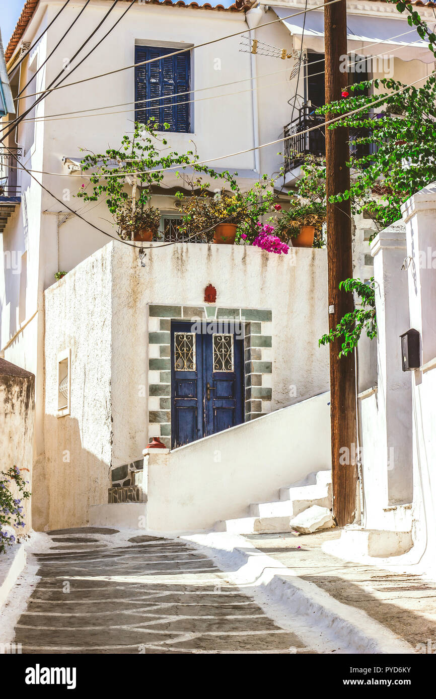 Narrow street in Neorio town on Poros island, Greece. Old white house with blue door and flowers Stock Photo
