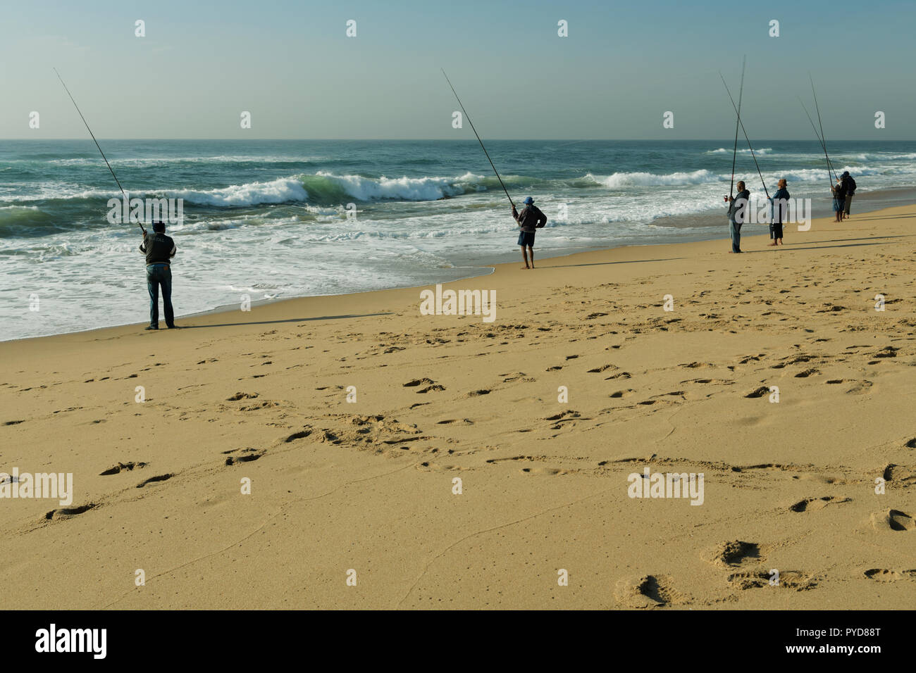 Durban, KwaZulu-Natal, South Africa, group, six adult fishermen holding fishing rods and standing on sandy beach at mid morning, The Bluff, landscape Stock Photo