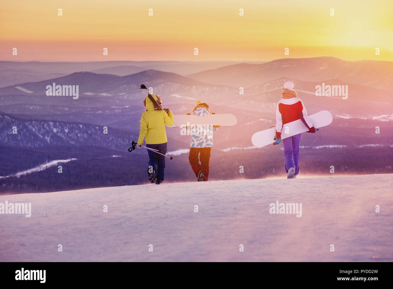Three friends skiers and snowboarders are walking on mountain top at sunset Stock Photo