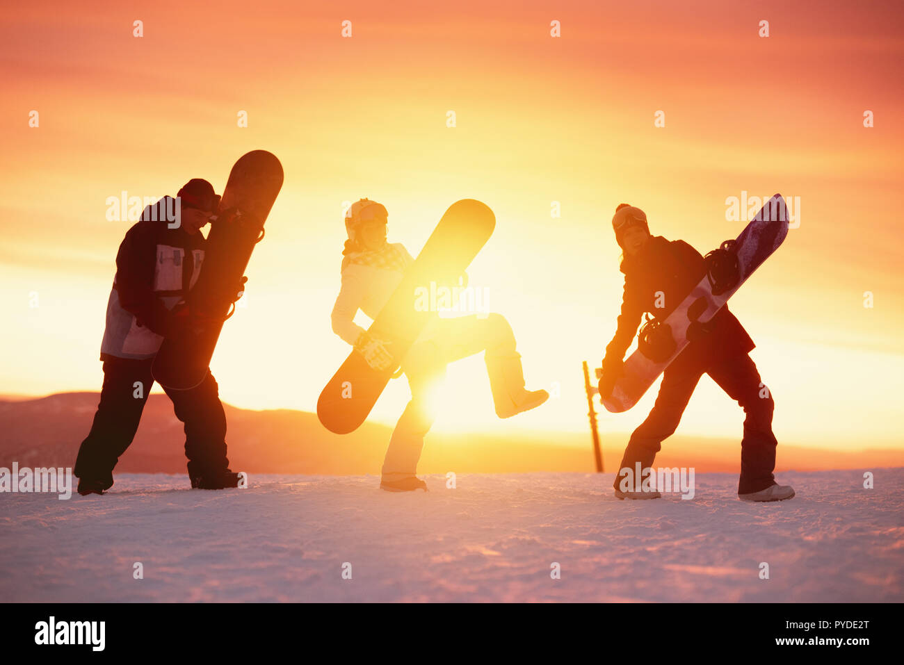 Three playful friends are having fun with snowboards. Funny silhouettes of snowboarders against sunset sky Stock Photo