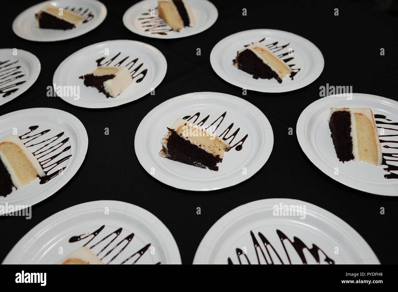 Plates of dark chocolate and vanilla cake drizzled with frosting at a reception. Stock Photo
