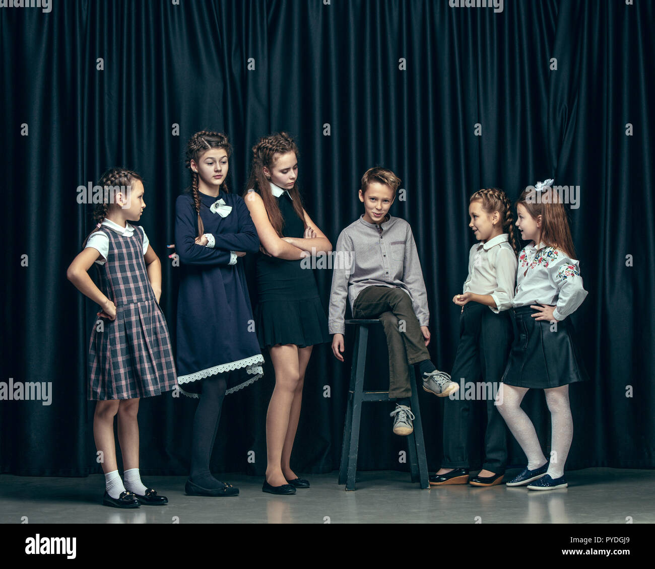 Cute surprised stylish children on dark background. Beautiful stylish teen  girls and boy standing together and posing on the school stage in front of  the curtain. Classic style. Kids fashion and emotions
