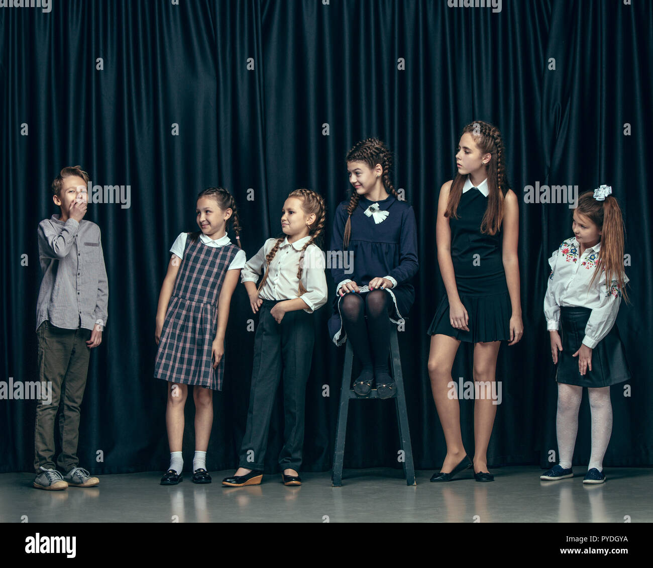Cute surprised stylish children on dark background. Beautiful stylish teen  girls and boy standing together and posing on the school stage in front of  the curtain. Classic style. Kids fashion and emotions