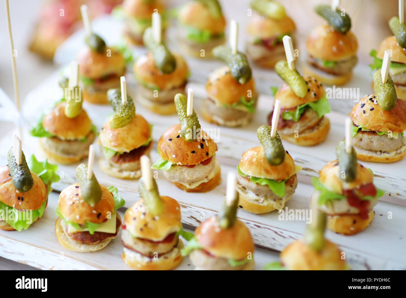 Delicious one bite mini burgers served on a party or wedding reception. Plates with assorted fancy finger food snacks on an event party or dinner. Stock Photo