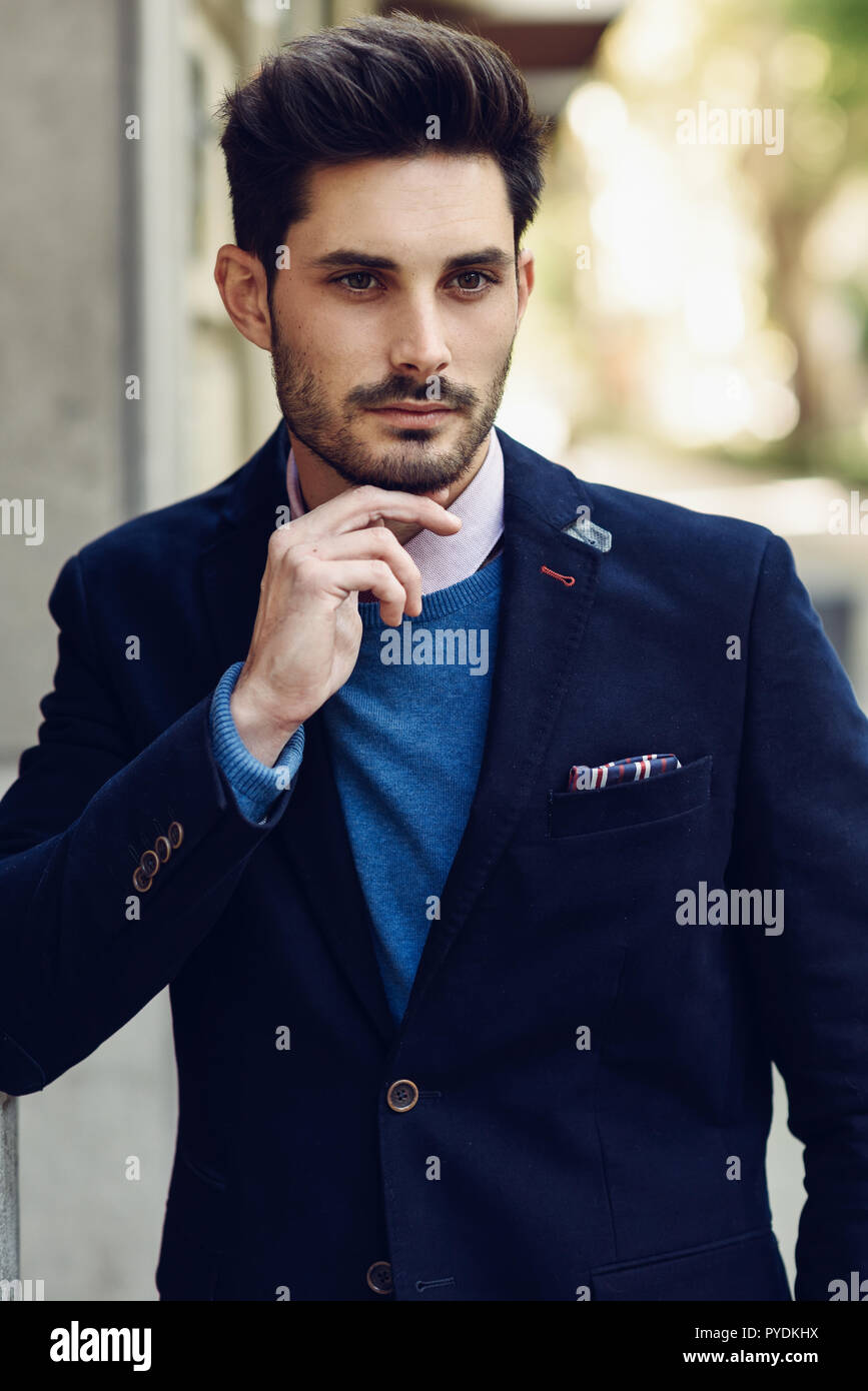 Attractive man in the street wearing british elegant suit. Young bearded  businessman with modern hairstyle in urban background Stock Photo - Alamy