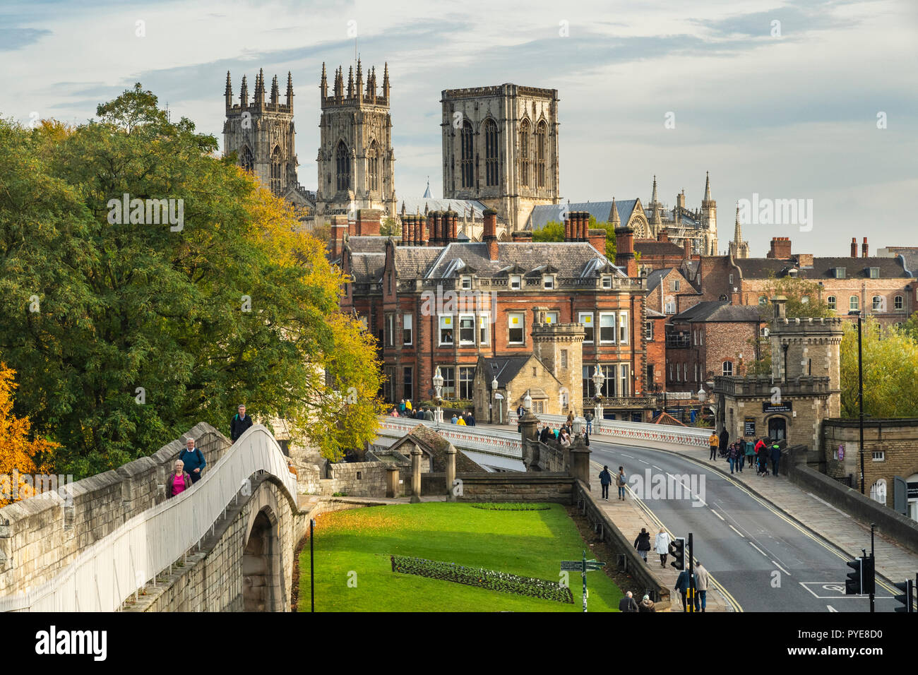 Scenic autumn York cityscape - historic landmarks, medieval walls, sunlit Minster towers, Lendal Bridge & people walking - North Yorkshire, England UK Stock Photo
