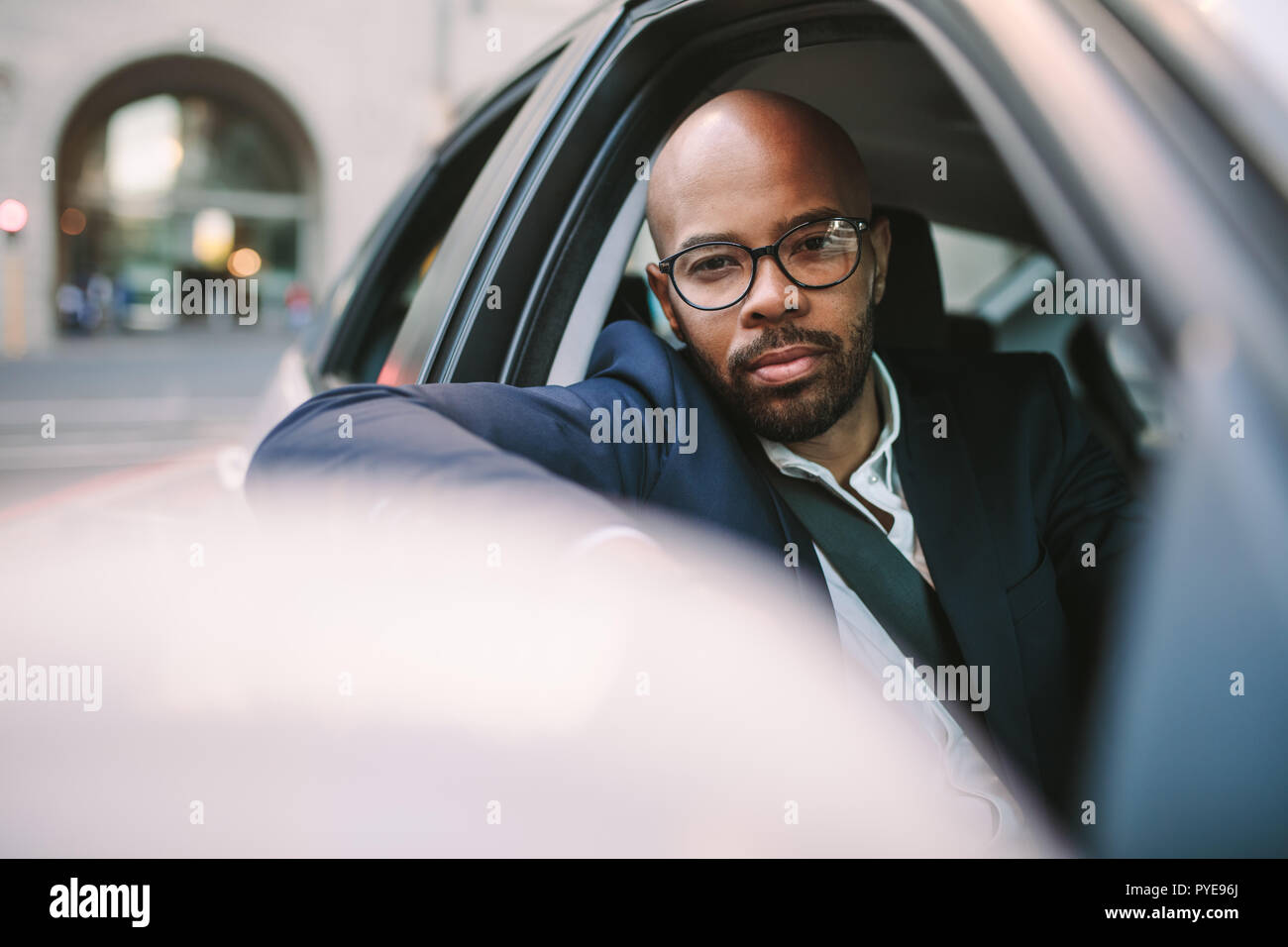 Handsome young black man in suit peeking out of car window while driving. African businessman driving car in the city. Stock Photo