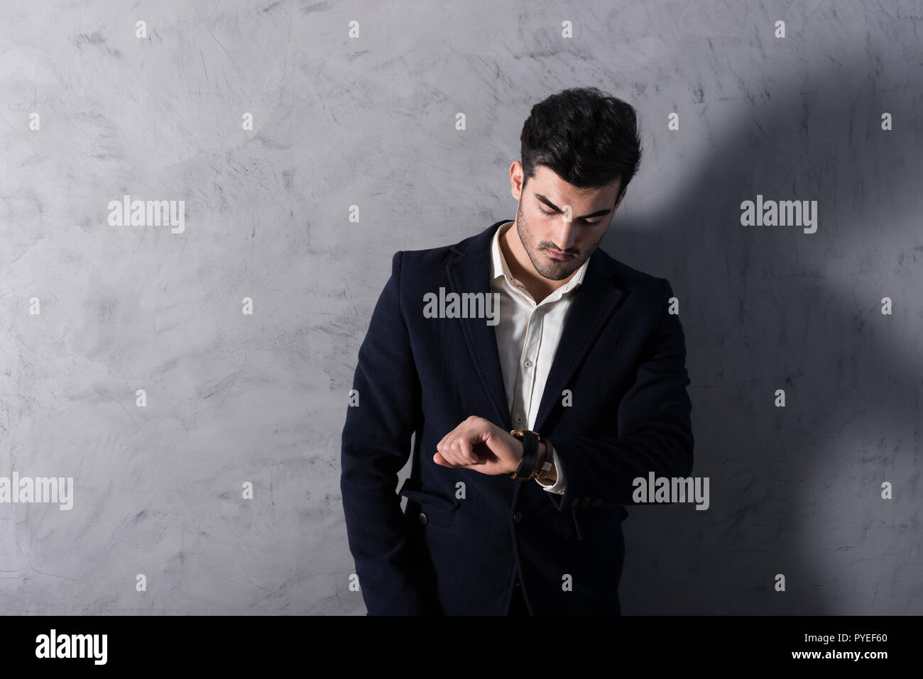 A serious handsome young businessman in a black suit checking the time ...