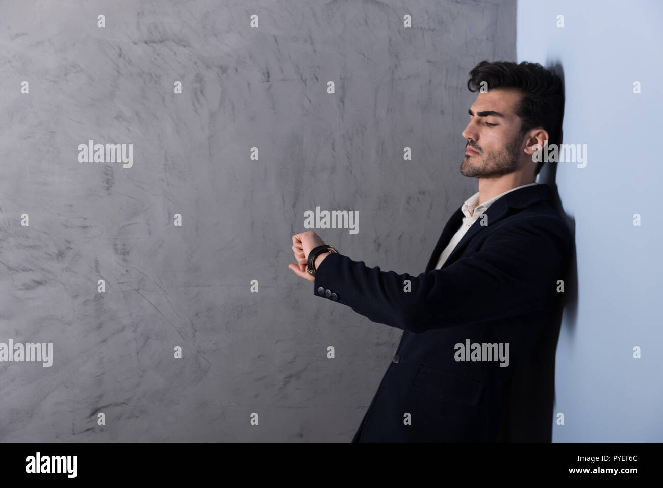 A serious handsome young businessman in a black suit checking the time ...