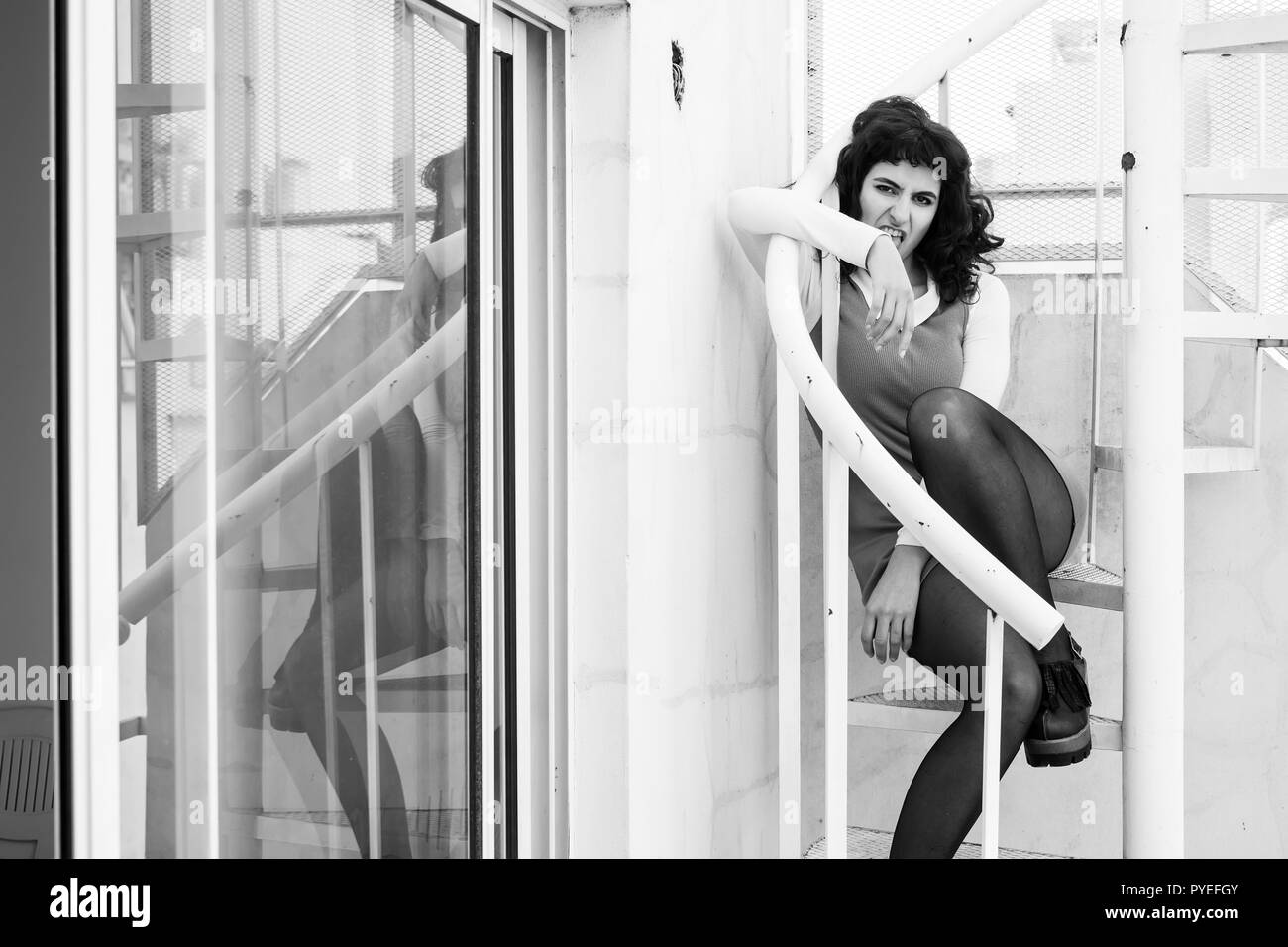 Portrait of a beautiful serious young woman in an elegant dress sitting on a metal stairs. Stock Photo