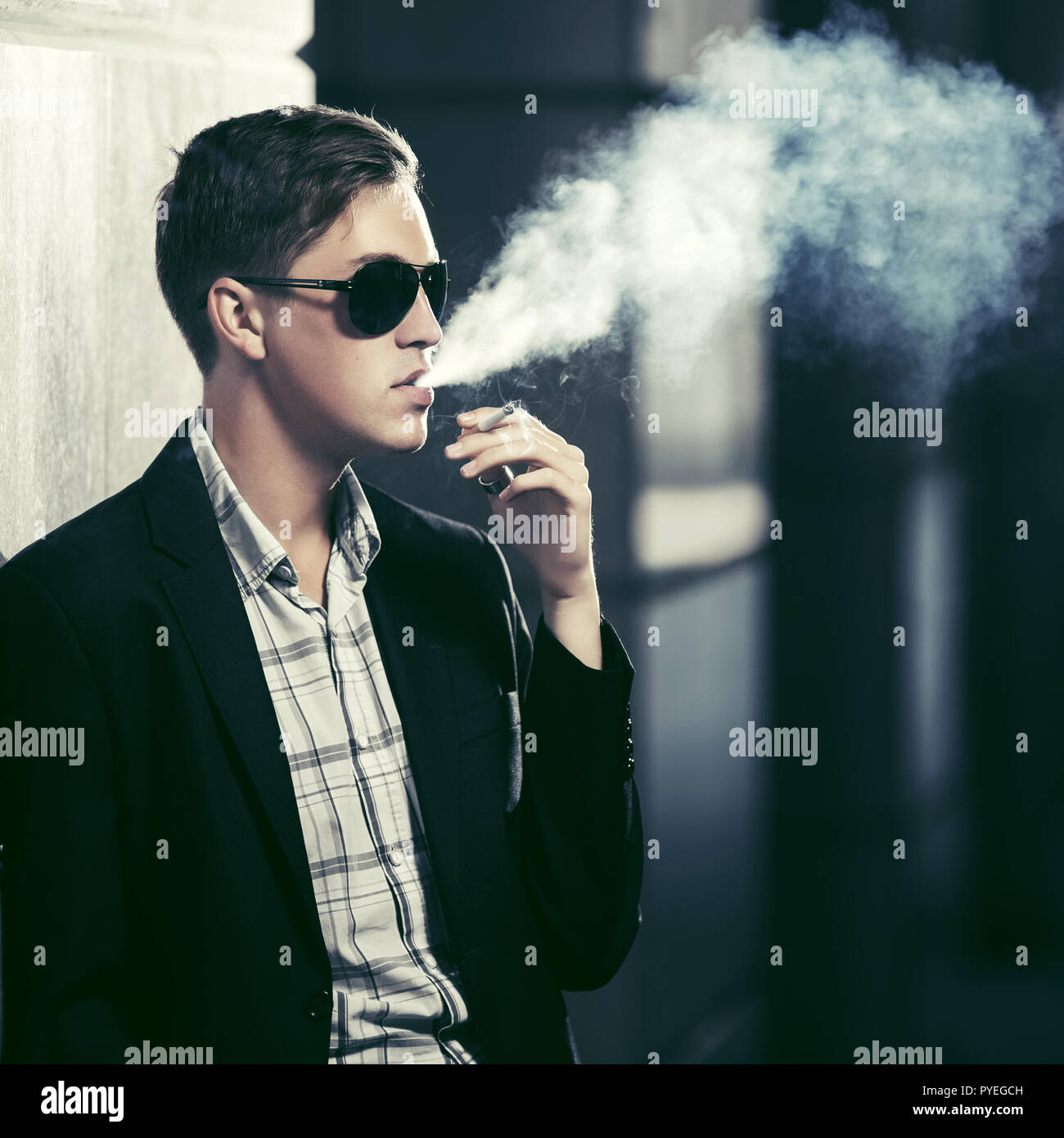 Young fashion man in sunglasses smoking a cigarette in night city street Stock Photo