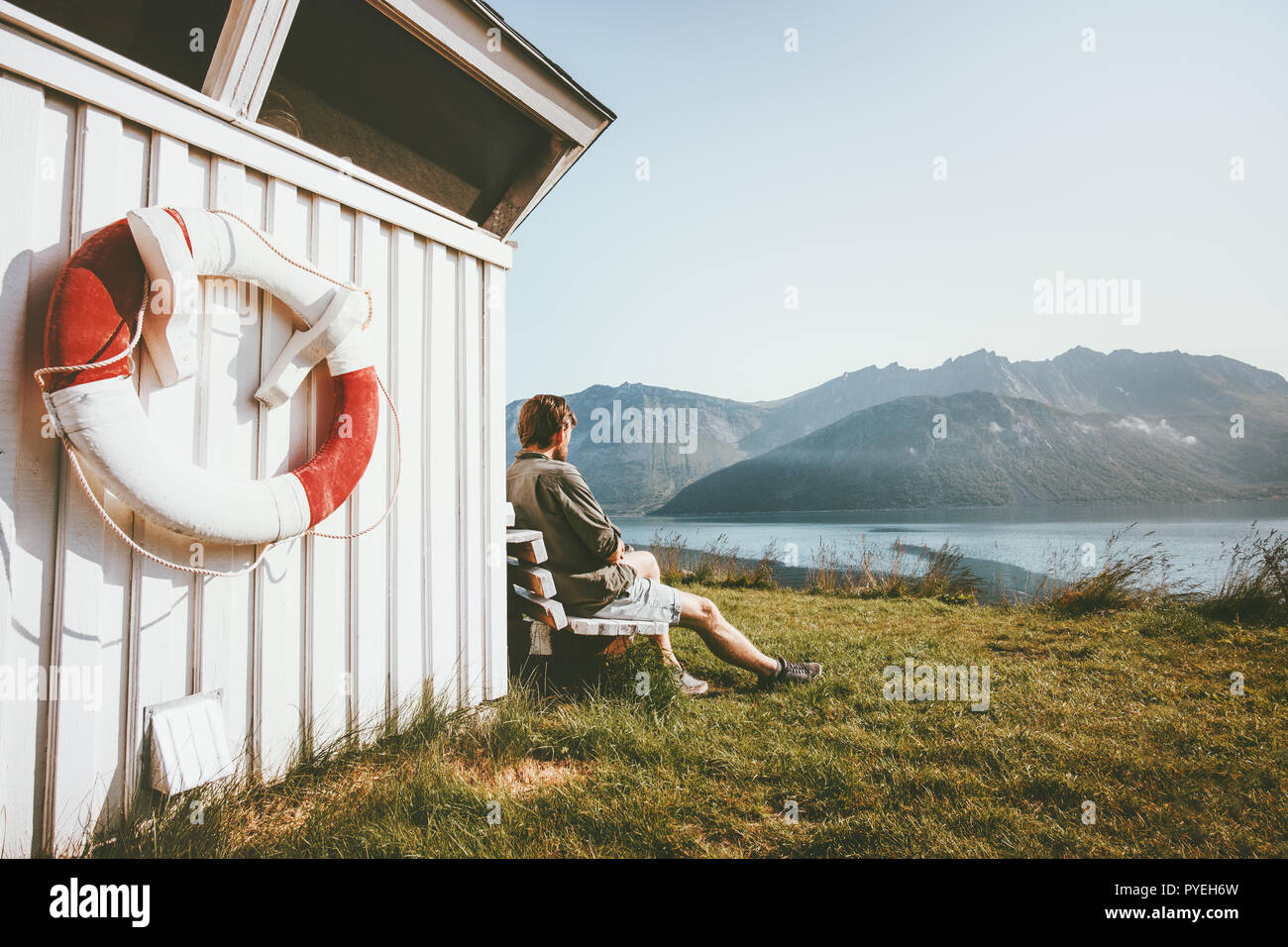 Man relaxing enjoying sea and mountain view outdoor near wooden house travel scandinavian vacations in Norway Stock Photo