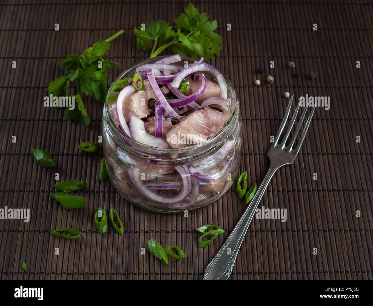 The fillet of salted herring, cut into pieces and sprinkled with ringlets of red onion, lies in a glass jar Stock Photo