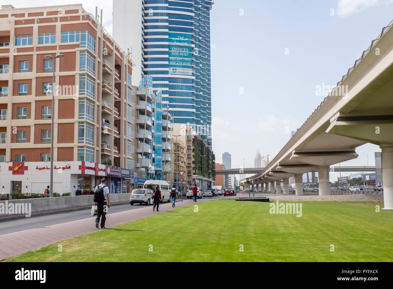People walking along an access road that runs parallel to Sheikh Zayed Road in the Al Barsha district next to the raised tracks of the Dubai Metro. Stock Photo