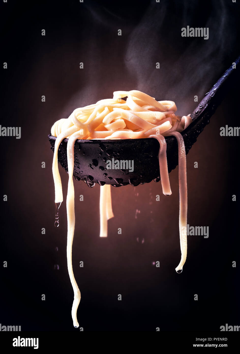 Steaming cooked fettuccine pasta on a black spoon and dark background Stock Photo