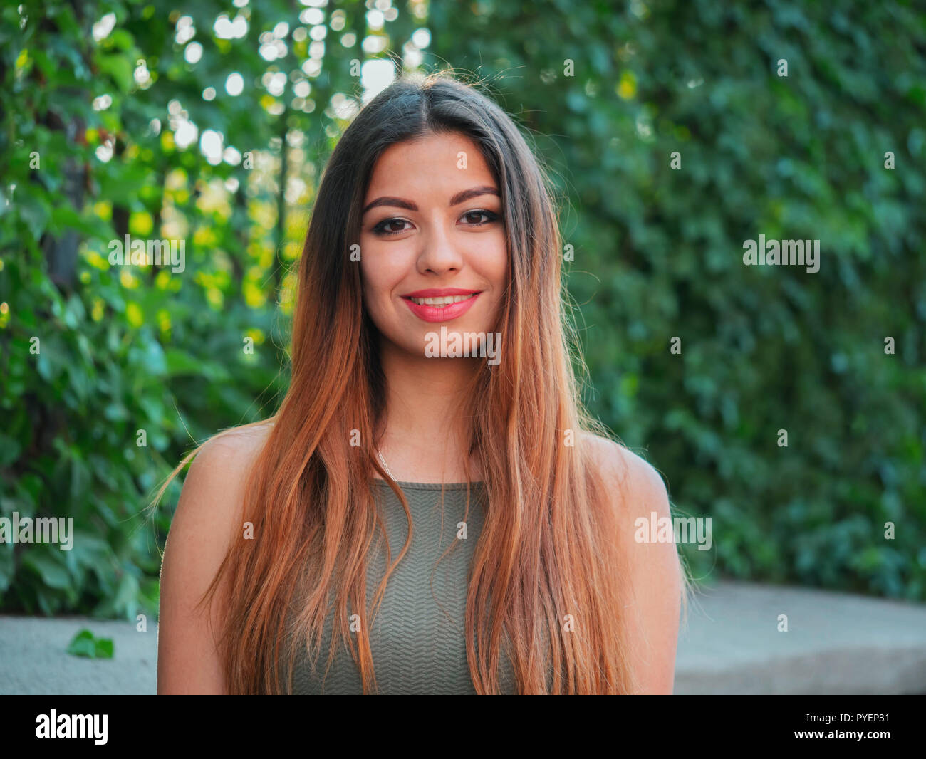 Portrait of young attractive girl looks into the camera with smile. Woman with oriental face, brown eyes and stylish ombre dyed long hairstyle on city Stock Photo