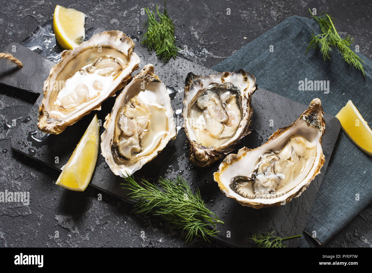 Opened Oysters with lemon on dark stone texture background Stock Photo